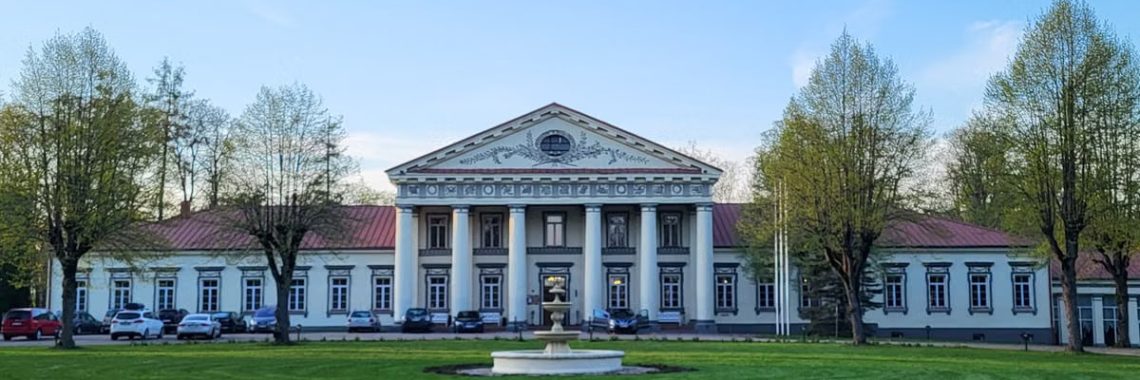 A scenic view of a neoclassical mansion surrounded by green lawns and trees in Lithuania.